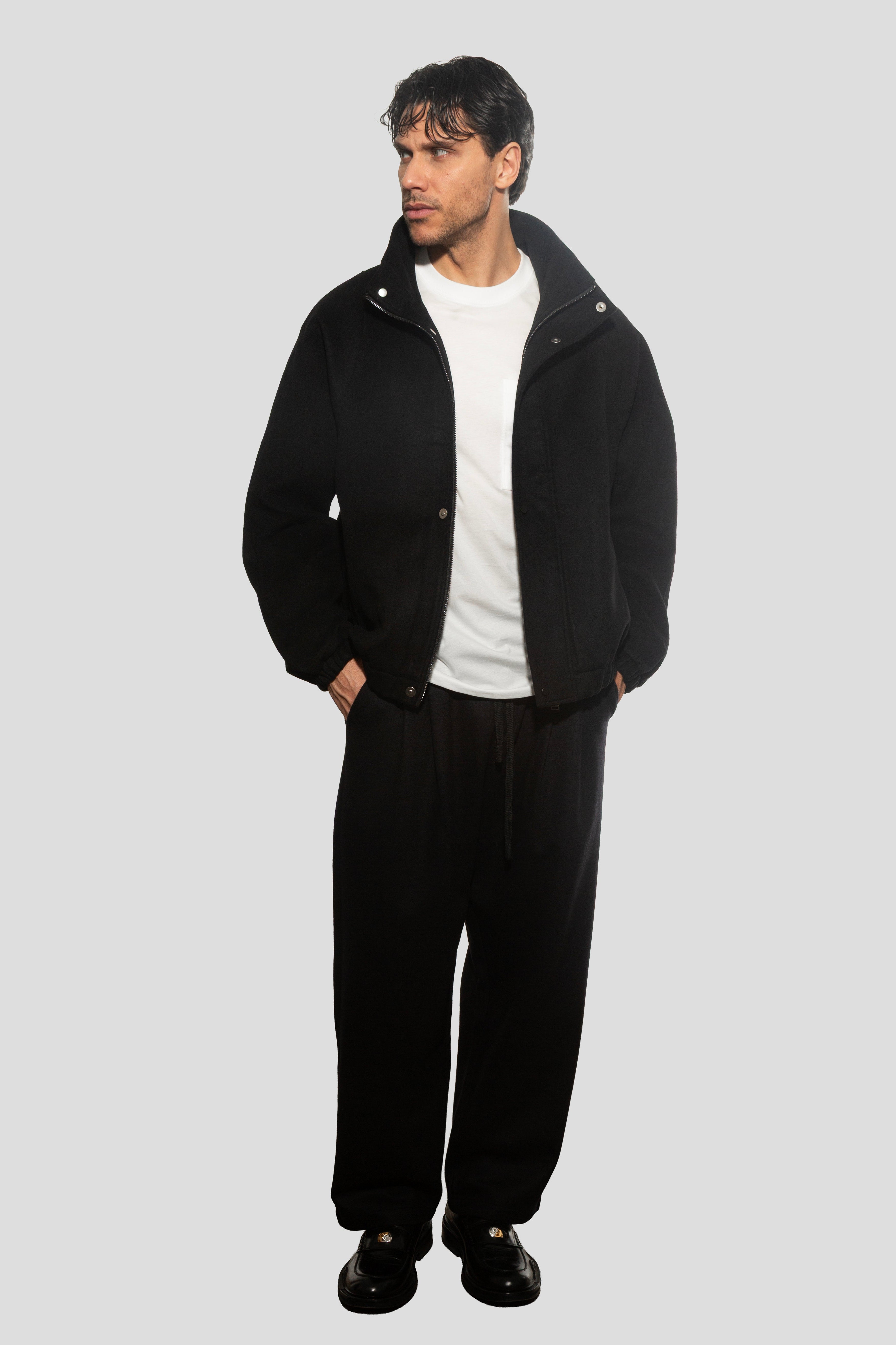 Man wearing a black coat and pants on a light gray background