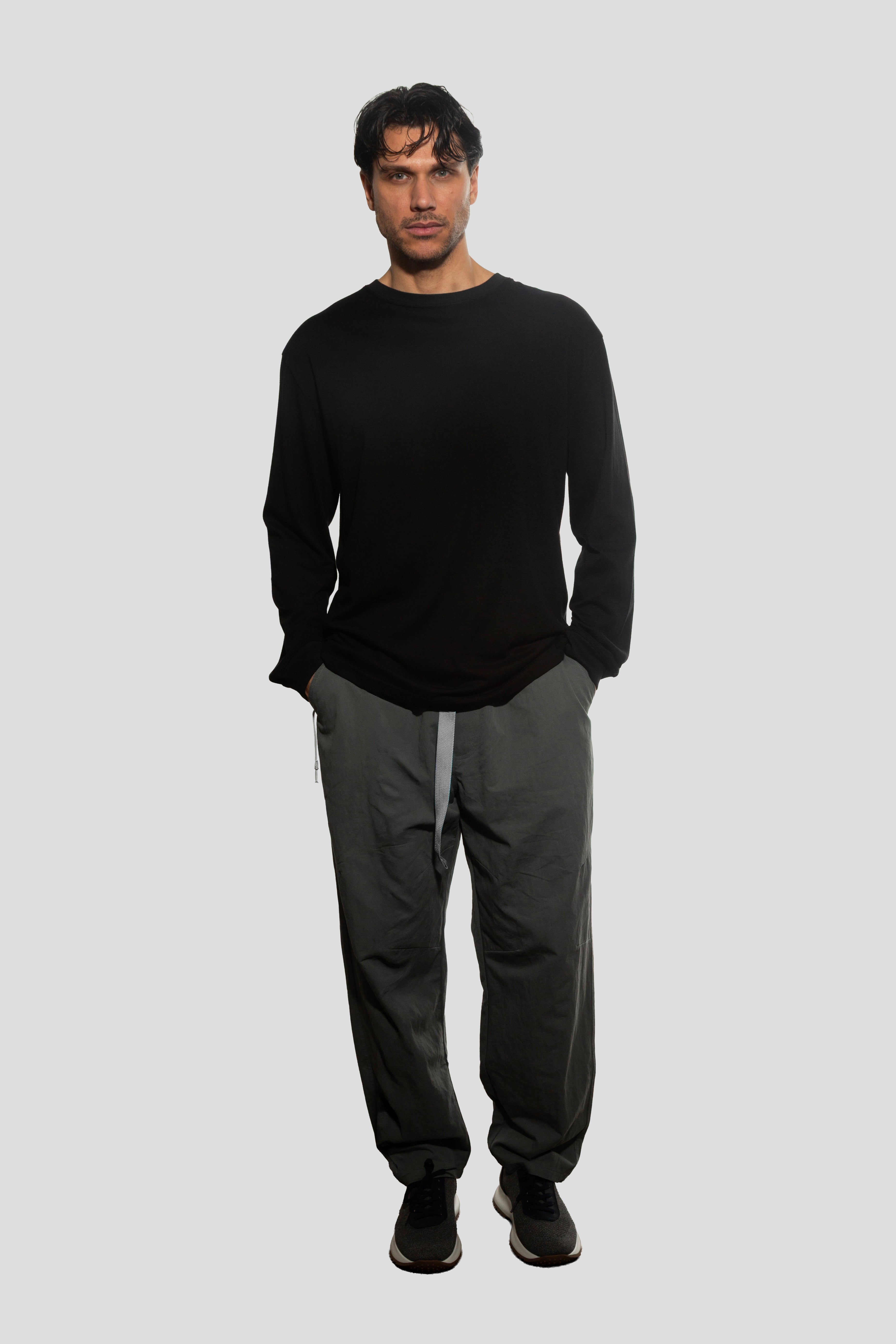 Man wearing a black long-sleeve shirt and gray pants on a white background