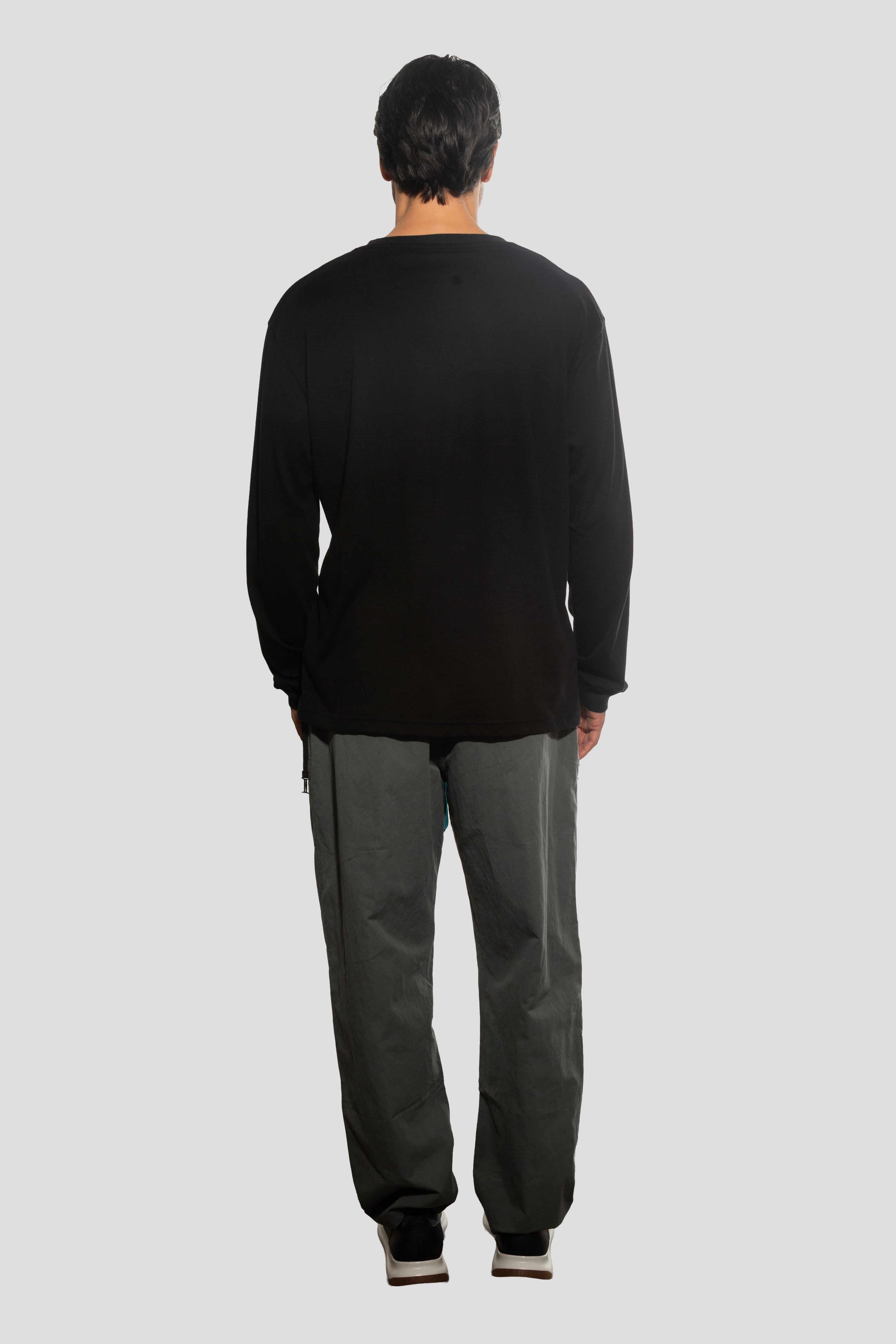 Person wearing a black sweater and gray pants on a light gray background