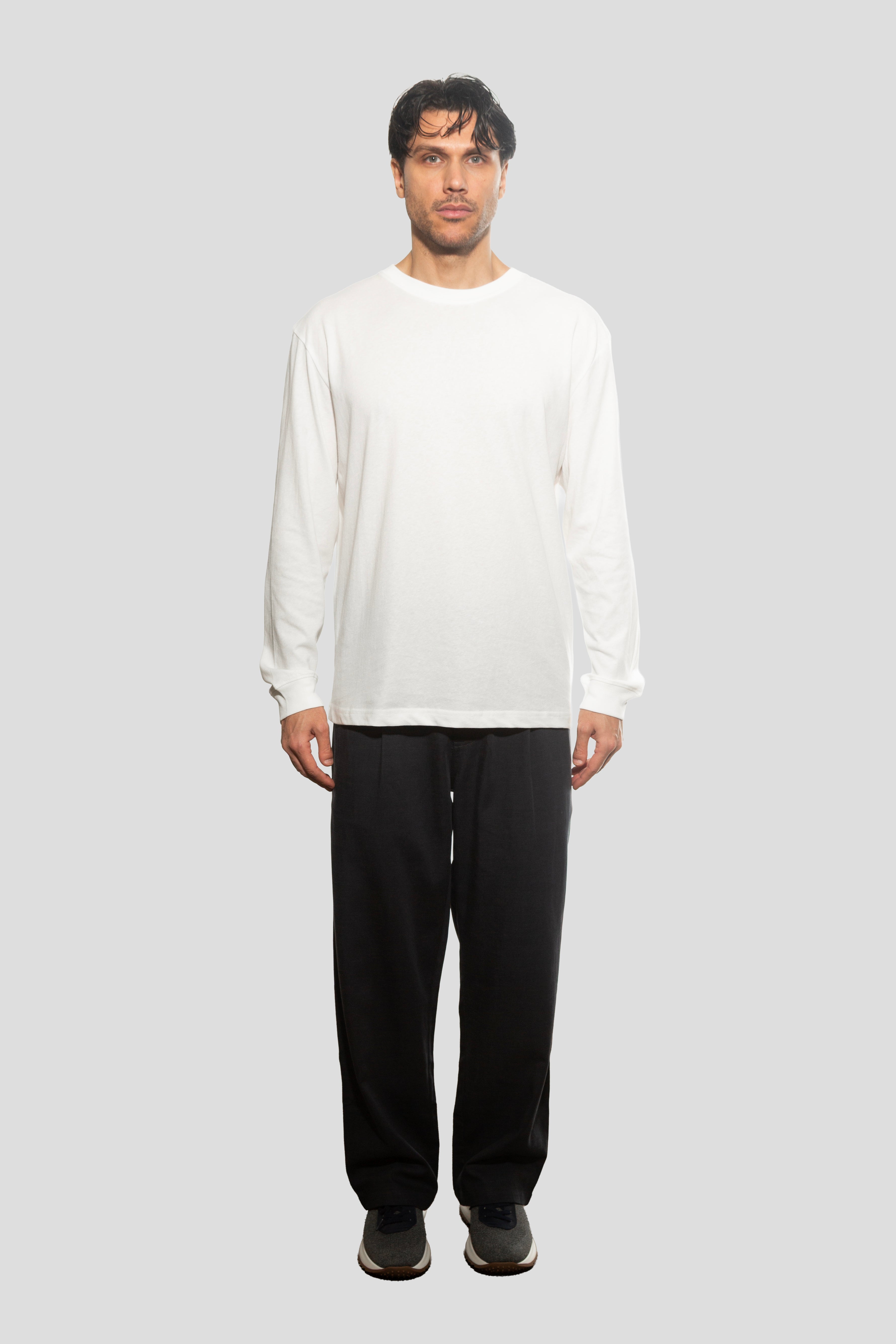 Person wearing a white long-sleeve shirt and black pants on a light gray background