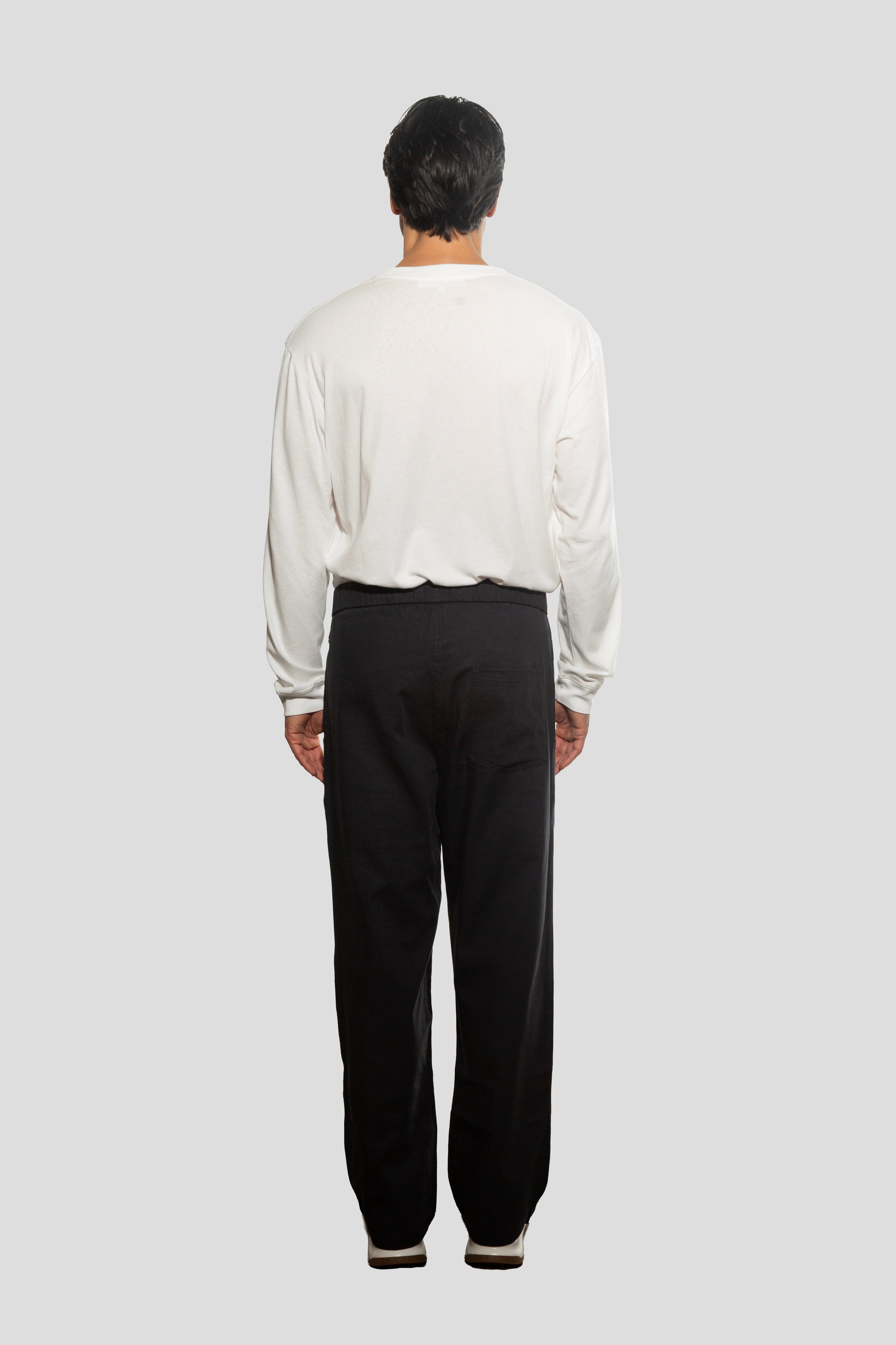 Person wearing a white shirt and black pants on a plain background