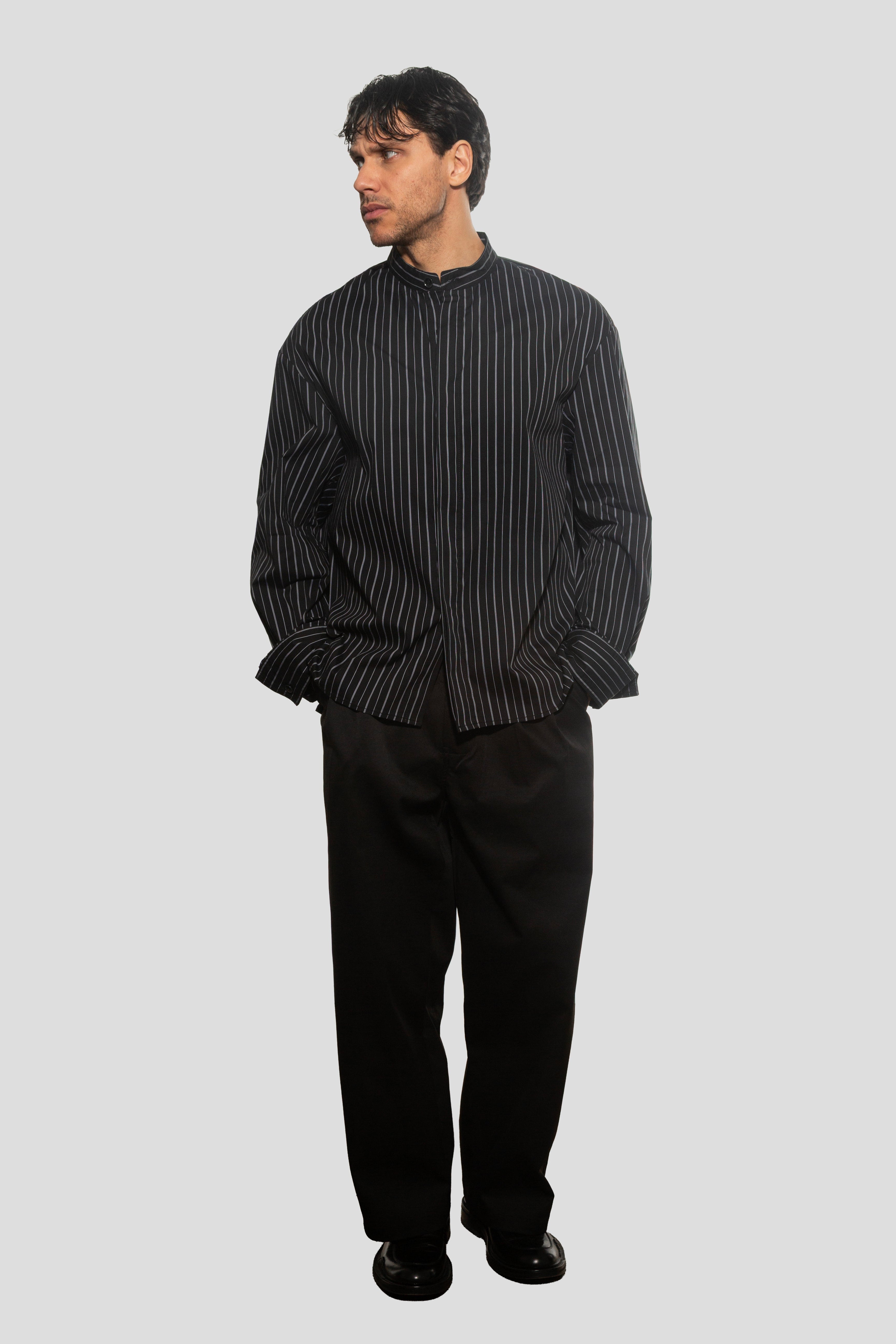 Man wearing a black and white striped shirt and black pants on a light gray background