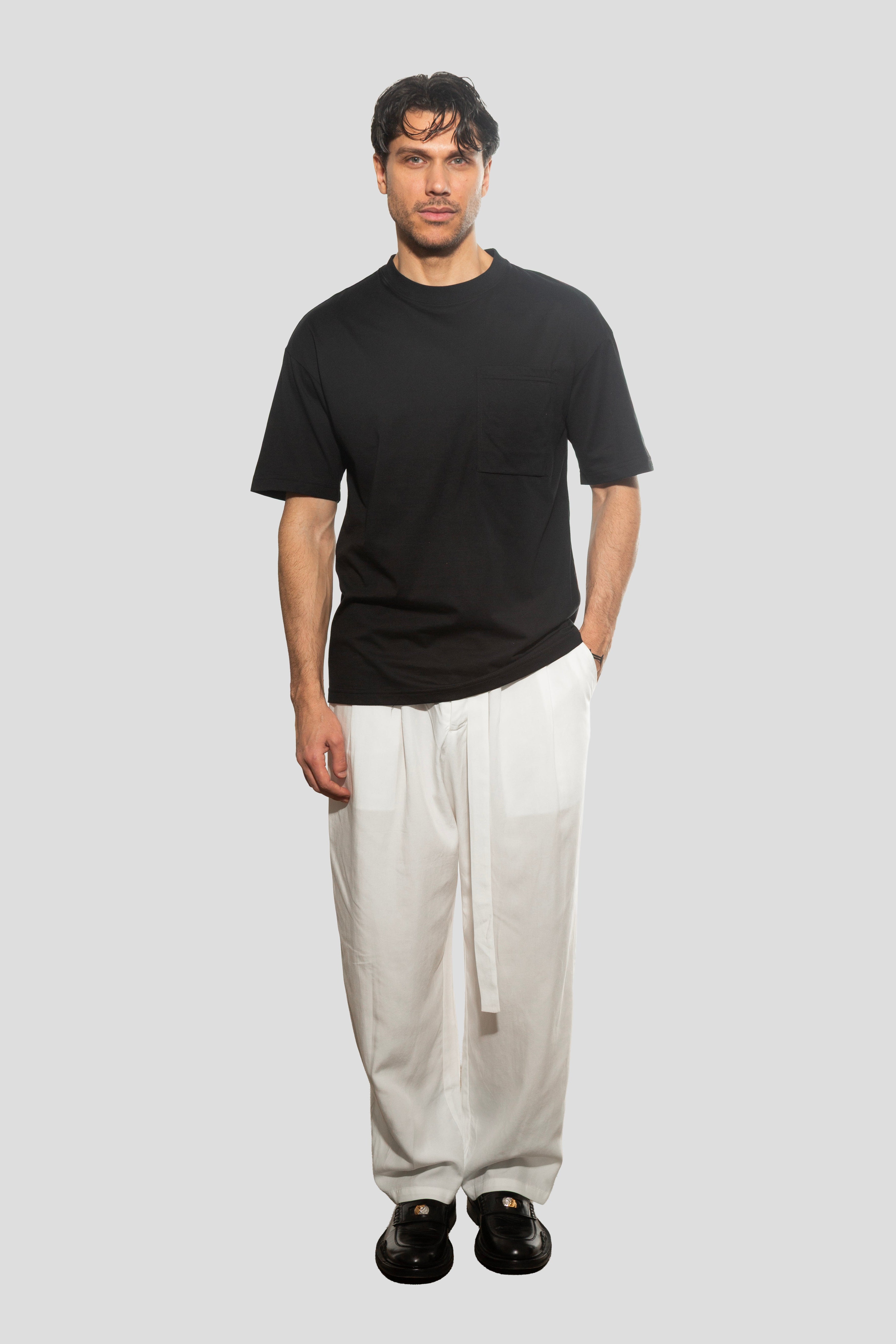 Man wearing a black t-shirt and white pants on a plain background