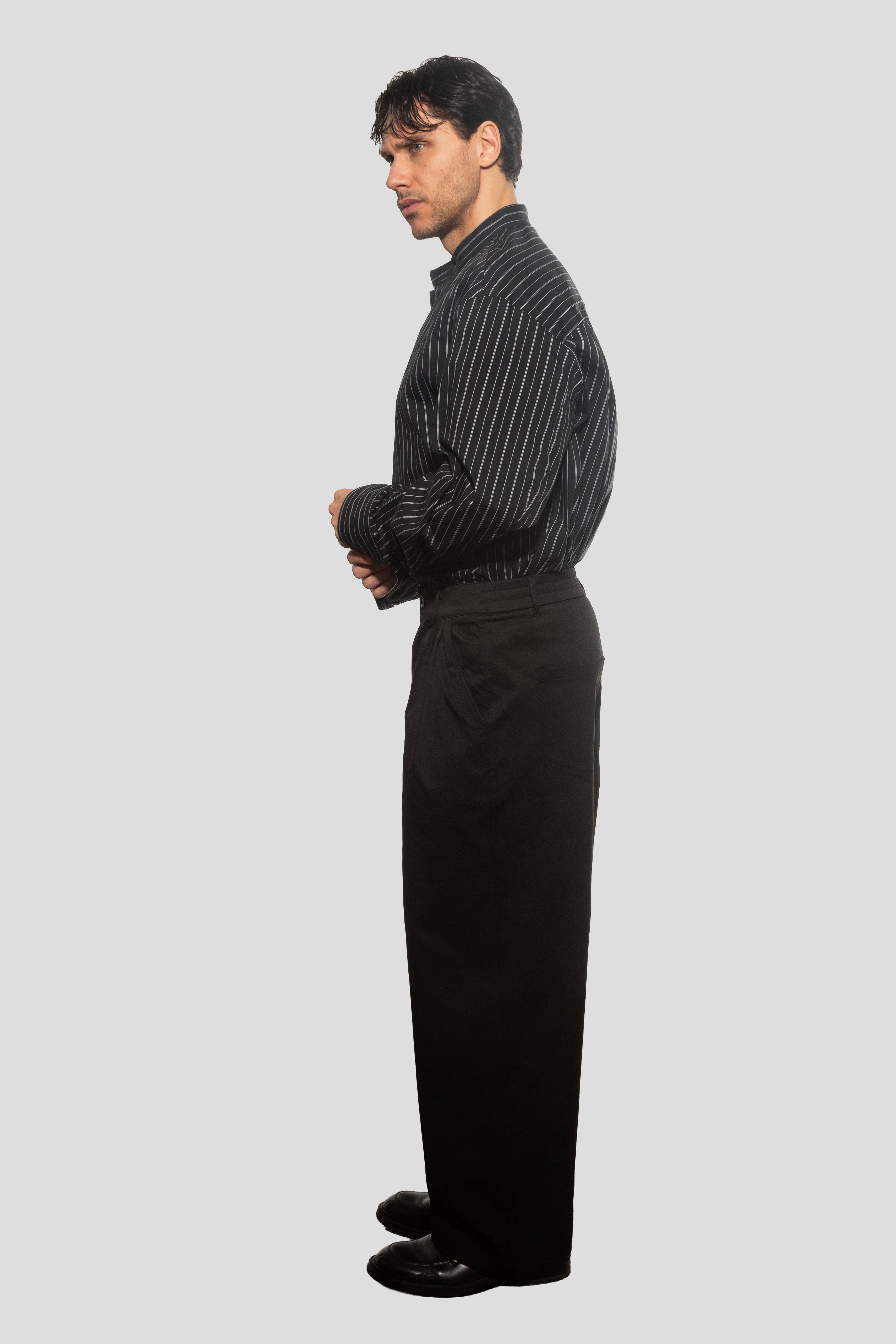 Man wearing a black pinstripe shirt and black pants on a light gray background