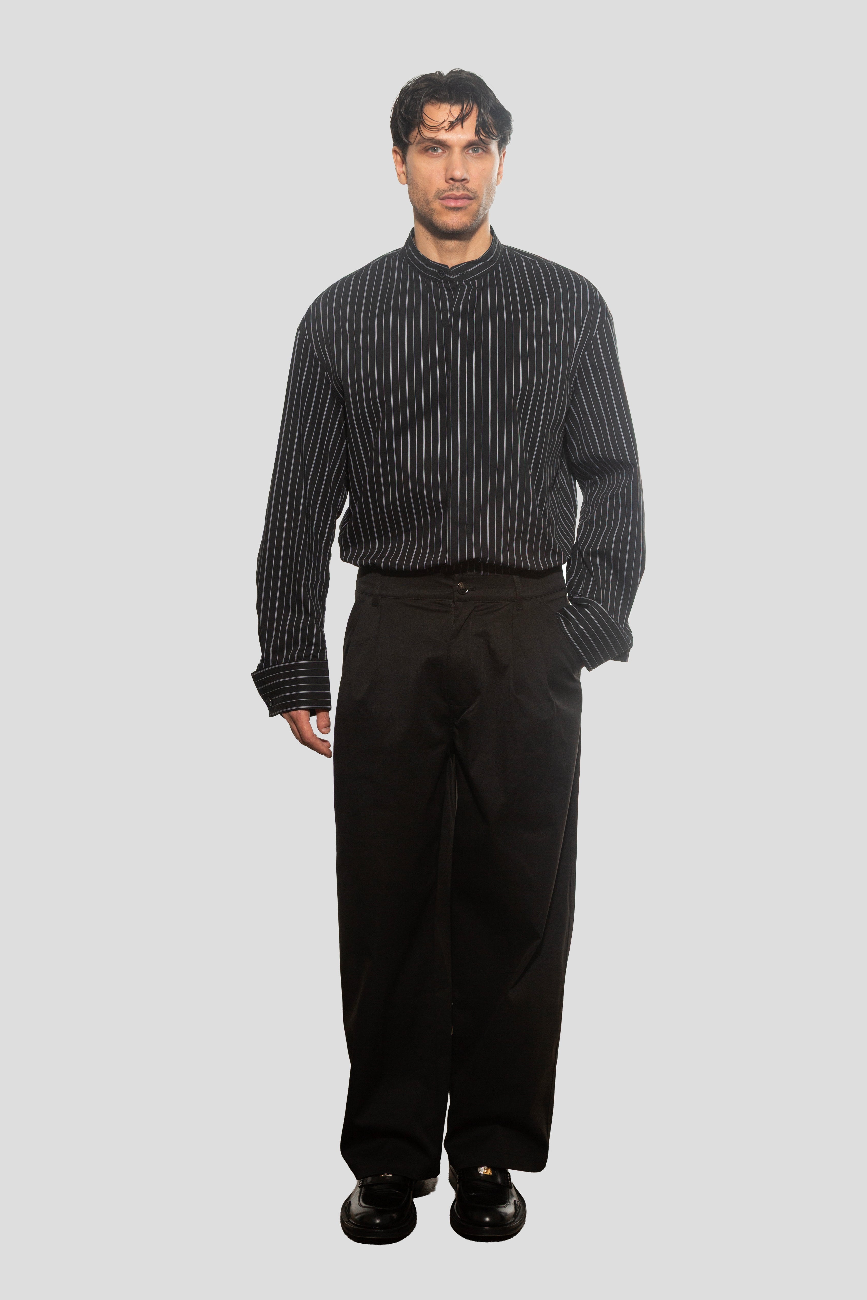 Man wearing a black and white striped shirt and black pants on a gray background