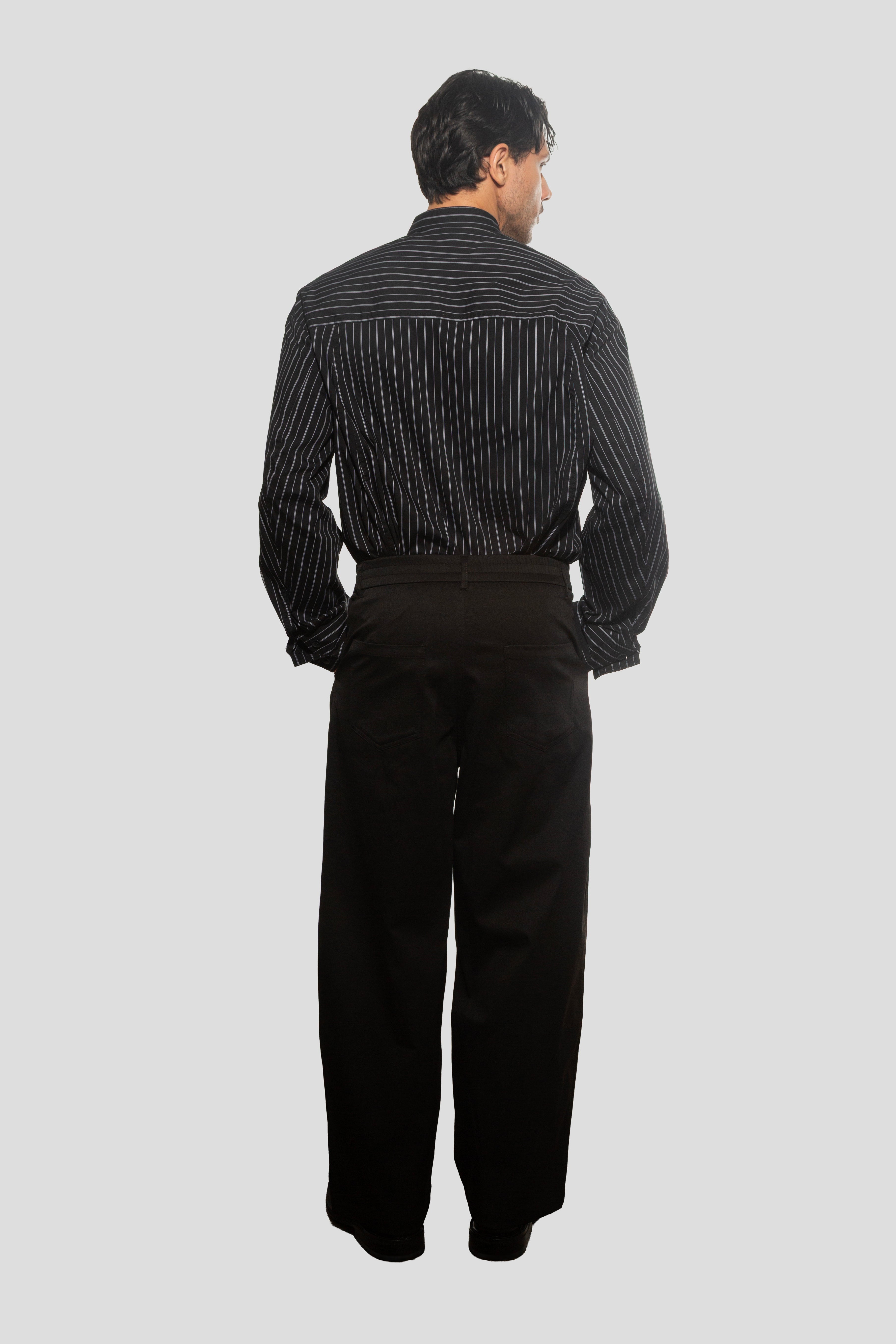 Man wearing a black and white striped shirt and black pants on a light gray background