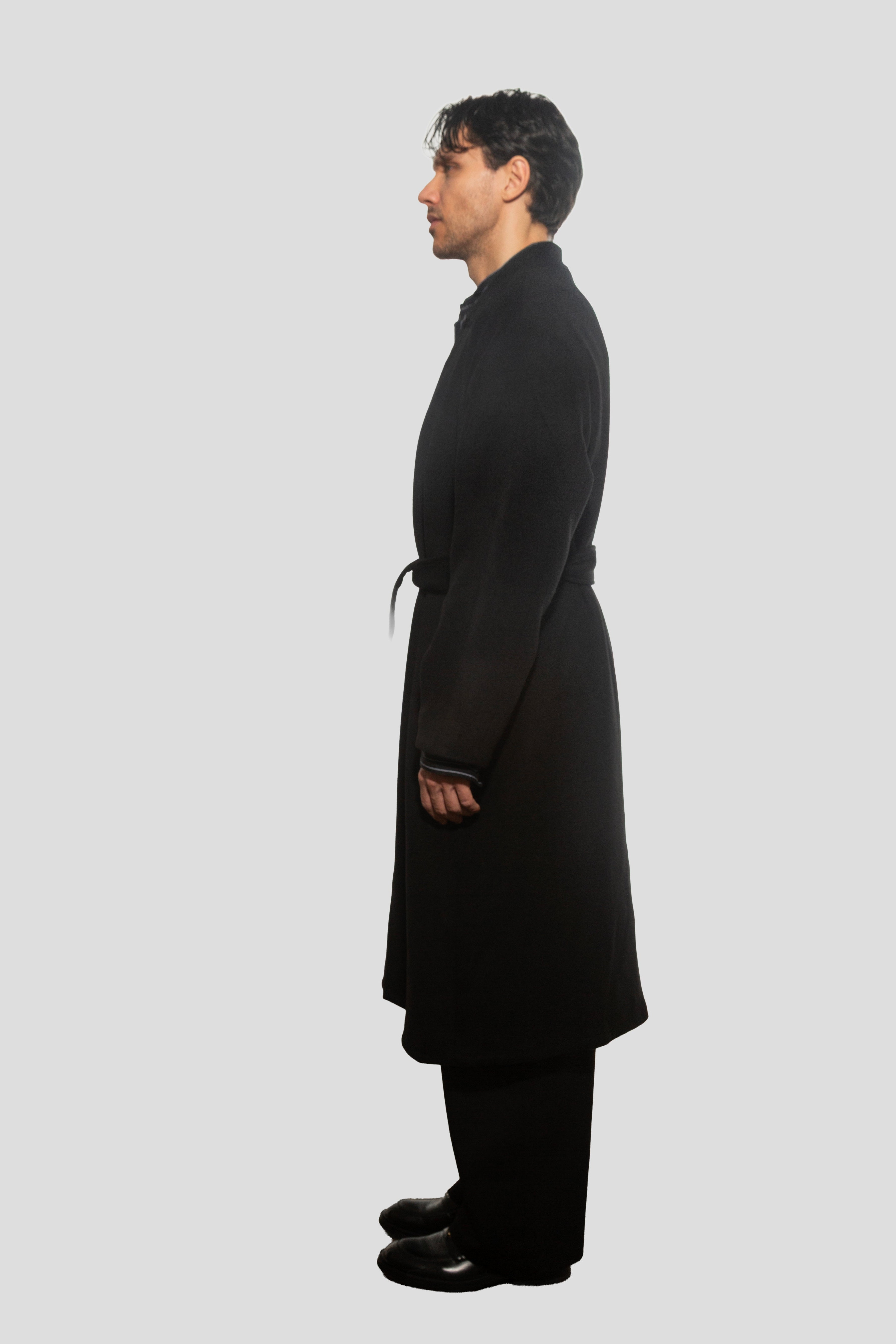 Man wearing a black coat standing against a white background