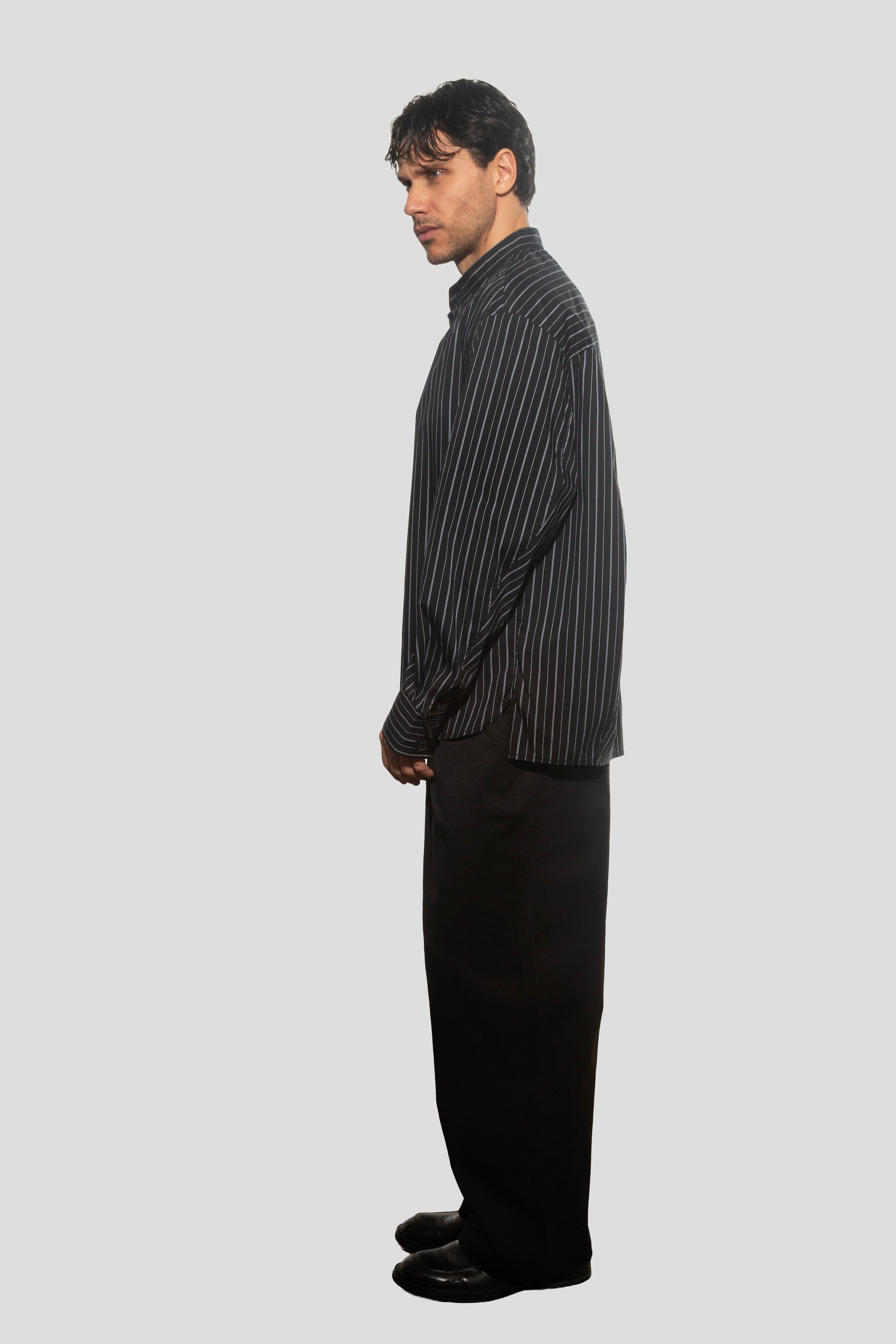 Man wearing a black and white striped shirt and black pants on a light gray background