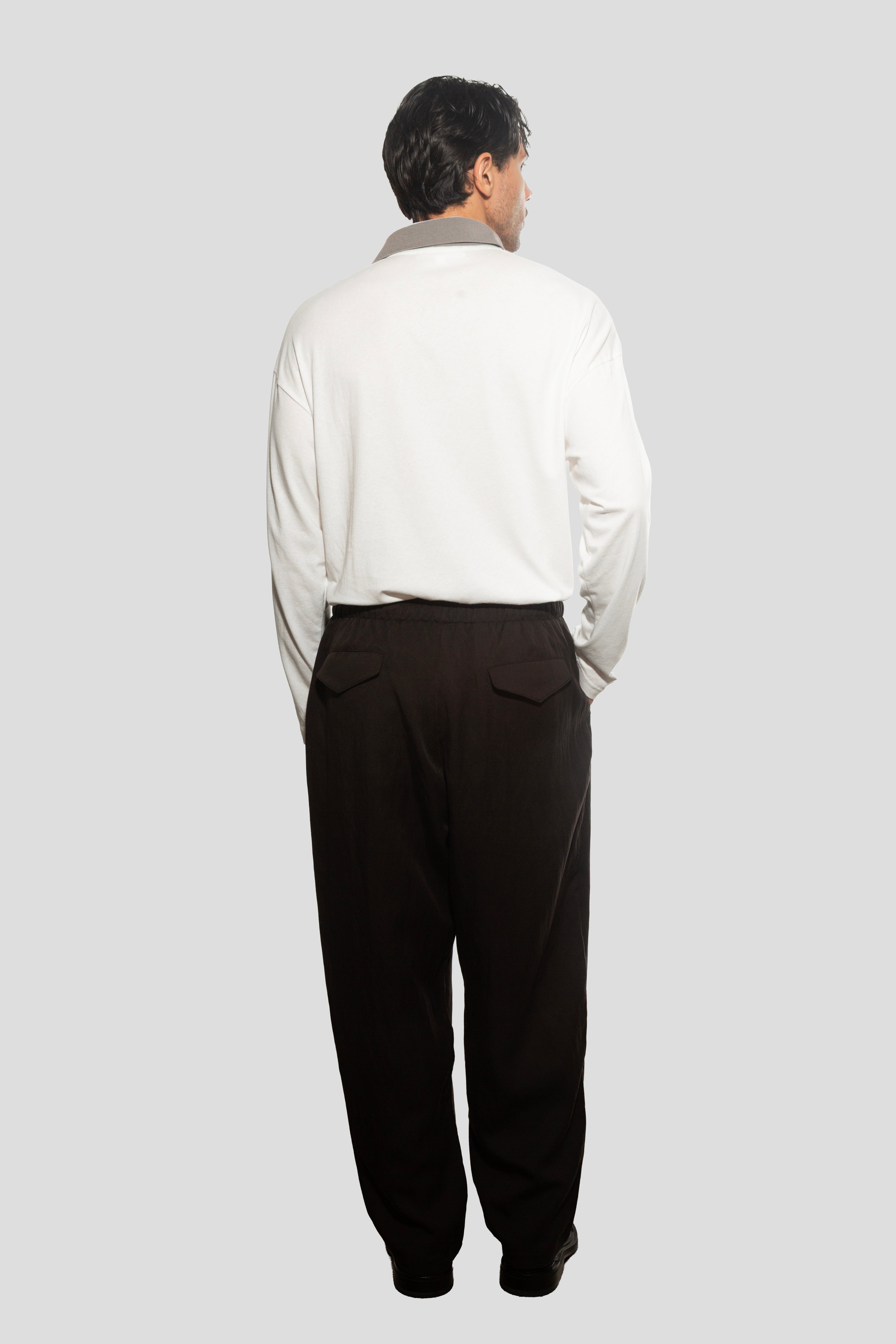 Man wearing a light-colored shirt and dark pants on a plain background